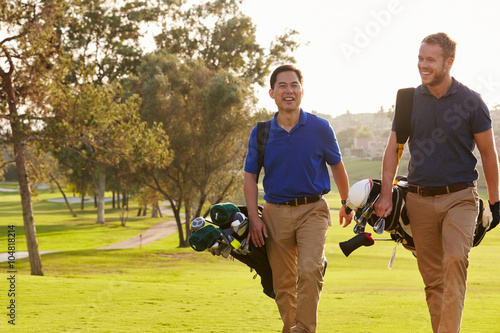 Two Male Golfers Walking Along Fairway Carrying Bags
