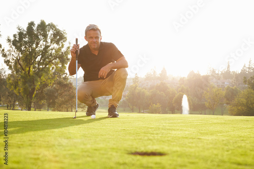 Male Golfer Lining Up Putt On Green