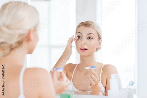 young woman putting on contact lenses at bathroom