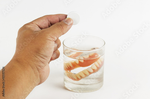 Hand holding cleaning tablets to a glass of False Teet