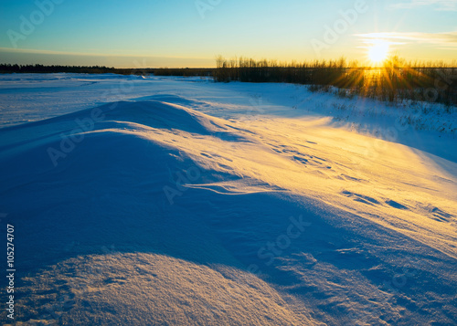 Winter landscape with the setting sun in snowy field.
