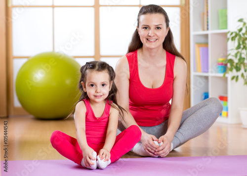 Young mother with little daughter exercising in gym at home