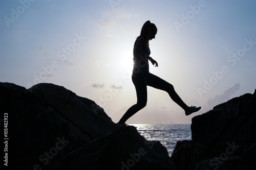 the young beautiful girl the sportswoman, in sportswear sneakers jumps through rocks at sunset, a high jump, physical training, fitness the instructor, an extreme sport, parkour,