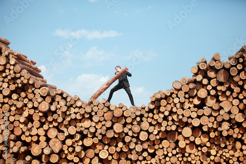 business vision - hardworking businessman on top of large pile of cut wooden logs