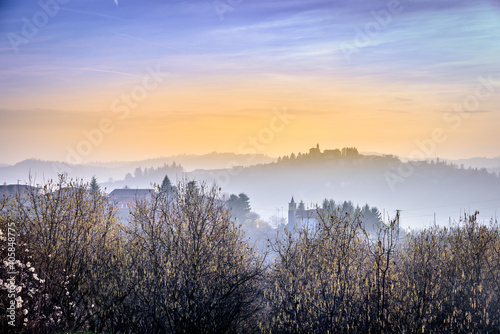 colorful sunset in Langhe hills with fog and houses far away