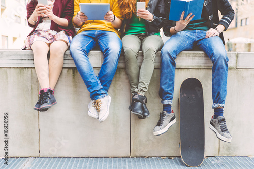 Group of teenagers making different activities sitting in an urb