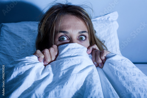 femme au lit cachée sous les draps apeurée