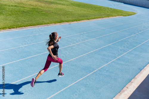 Runner sprinting towards success on run path running athletic track. Goal achievement concept. Female athlete sprinter doing a fast sprint for competition on blue lane at an outdoor field stadium.