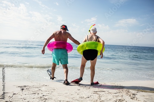 Senior couple in inflatable ring walking towards sea