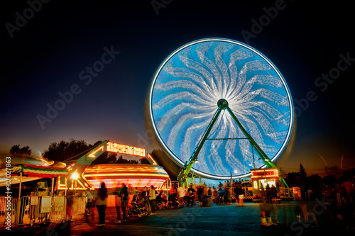 Spinning Ferris wheel at night with a black sky at the county fair with people in the foreground