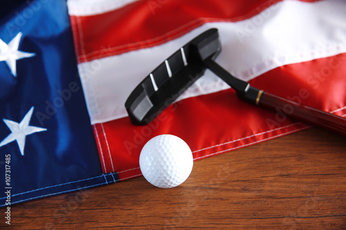 Golf ball, club and American flag on wooden table. Popular sport concept