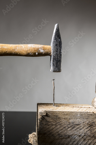 Martello che batte su chiodo su legno - sfondo chiaro grigio