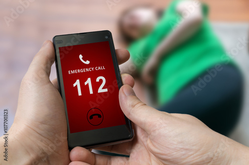 Man dialing emergency (112 number) on smartphone. Woman had heart attack and is lying on the floor.
