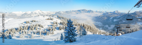Alpine ski slope mountain winter panorama with ski lift,skiers and snow covered forest.
