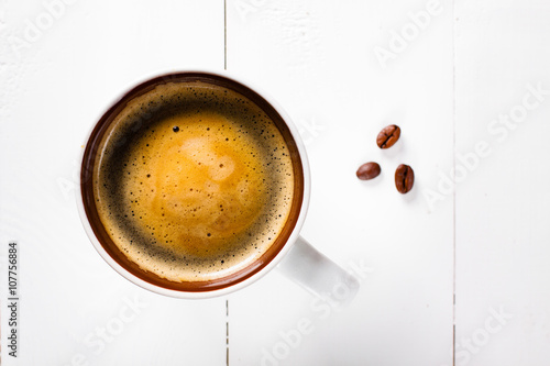Coffee cup top view on white wooden table background. Flat lay cup of coffee and three coffee beans.