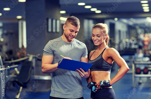 smiling young woman with personal trainer in gym