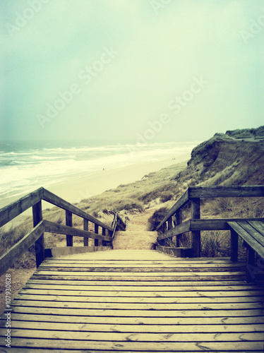 Lonely footpath or wooden stairway through a beach dune. Beach on Sylt with stormy sky