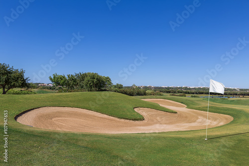 Sand trap on golf course with a white flag.