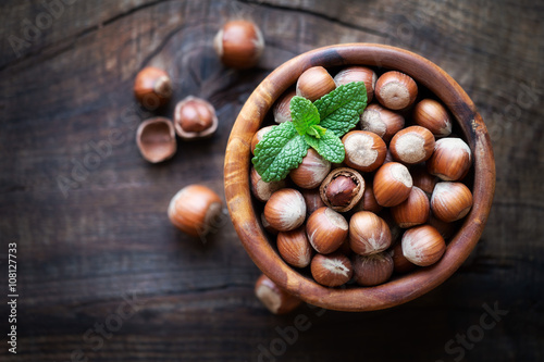 Shelled hazelnuts in a wooden bowl against dark rustic wooden background. Overhead view with shallow depth of field
