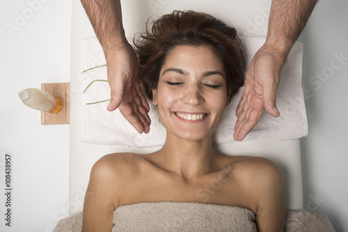 Massaggio al viso a bellissima donna sorridente distesa su un lettino di un centro benessere.