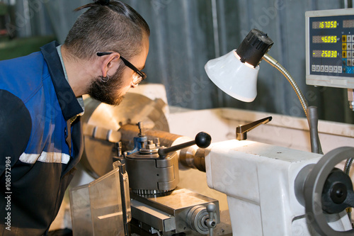 metalworking industry: machinery repairman worker processing metal piece at lathe machine in factory workshop