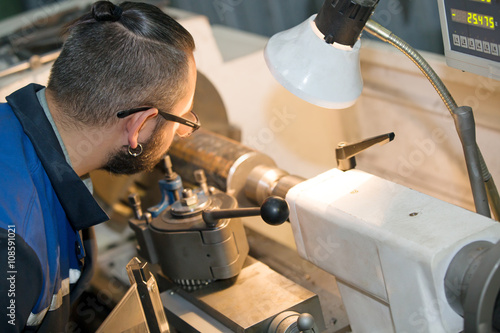 metalworking industry: factory man worker in uniform working on lathe machine in workshop