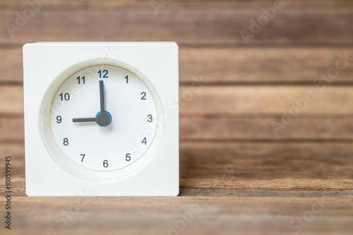 Closeup white clock showed nine o'clock on blurred brown wood board background