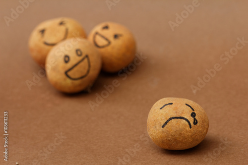 A group of brown ball laughing in the background while the brown ball in front alone and look sad and depressed. Concept of discrimination,bully,mental illness. 