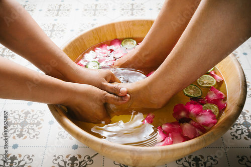 Closeup shot of a woman feet dipped in water with petals in a wooden bowl. Beautiful female feet at spa salon on pedicure procedure. Shallow depth of field with focus on feet. 