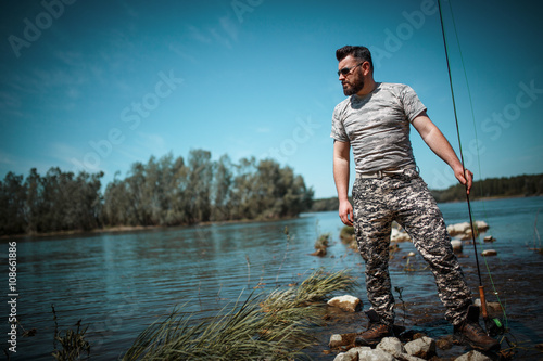 Fly fisherman in camouflage standing next to the river.
