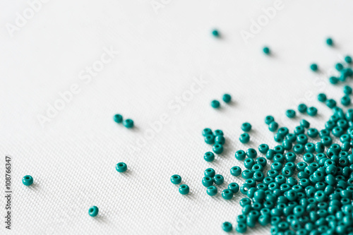 Scattered seed beads of emerald color on the textile background 