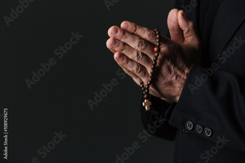 Hands of priest holding rosary and praying