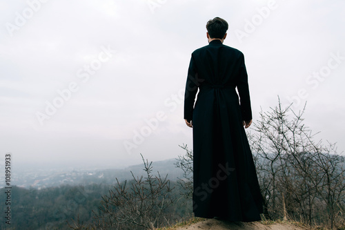 Portrait of handsome catholic bearded man priest or pastor posing outdoors in mountains