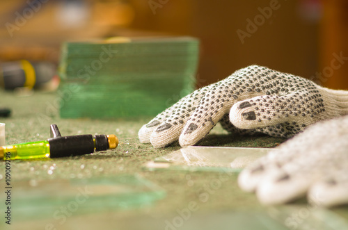 Closeup hands wearing white working gloves holding table edge, handheld cutting engravement tool for glass lying in front