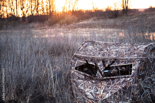 Hunting tent with hunters lurking waiting for prey in the field next to the river while picturesque sunrises