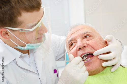 Closeup portrait of young dentist treating senior elderly man