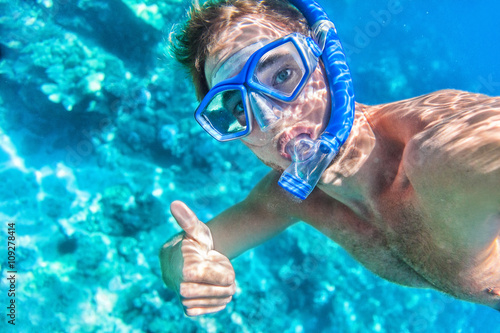Snorkeling man underwater giving thumbs up ok signal wearing snorkel and mask having fun on beach summer holidays vacation enjoying recreational leisure time swimming in the sea.