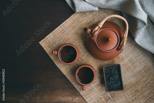 Chinese Tea Ceremony. Brown ceramic teapot and brown tea cup .Green tea on bamboo mat on aged wooden table. Top view.