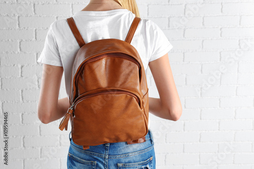 Back of woman with brown leather backpack against white brick wall background