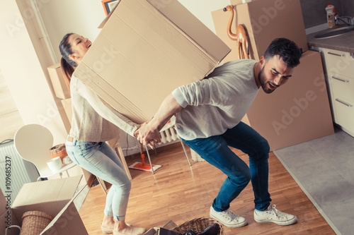 Young married couple carrying big cardboard box into new home. Moving house. 