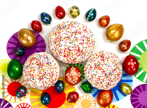 Традиционный Пасхальный кулич и крашеные яйца с украшениями на разноцветном фоне. 