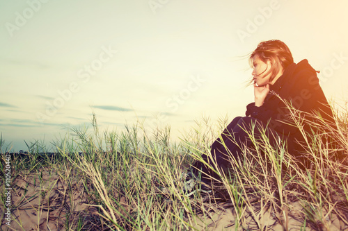 Sad young girl sitting alone on a grass outdoors,Sadness. Loneli