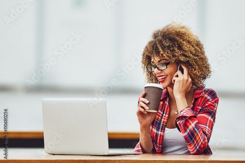 Young woman working on laptop and talking on mobile phone 