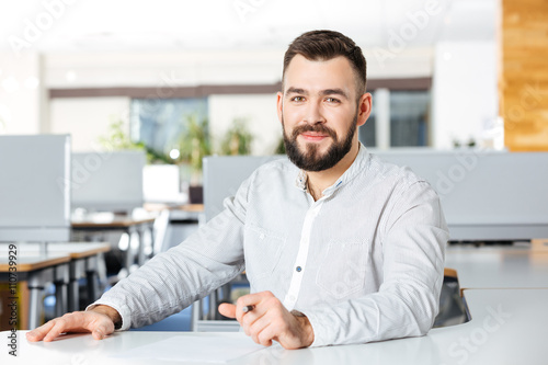 Smiling bearded businessman sitting and writing in office