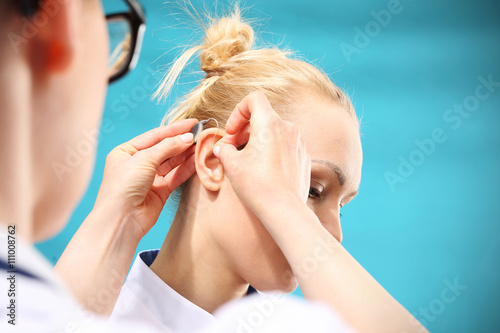 Aparat słuchowy.Lekarz zakłada kobiecie aparat słuchowy na ucho 