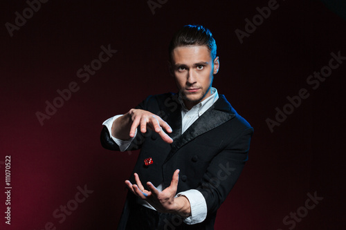 Confident young man magician showing tricks using one flying dice