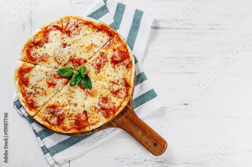 Hot true PEPPERONI ITALIAN PIZZA on towel with salami and cheese. TOP VIEW Tasty traditional pepperoni pizza on board on white wooden table. Copy space for your logo. Ideal for commercial 