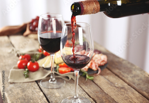 Pouring red wine into glass on wooden table closeup
