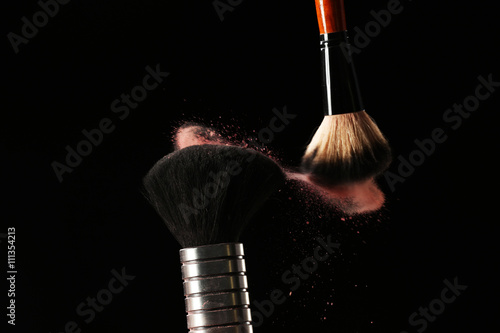 Two make up brushes with powder on black background