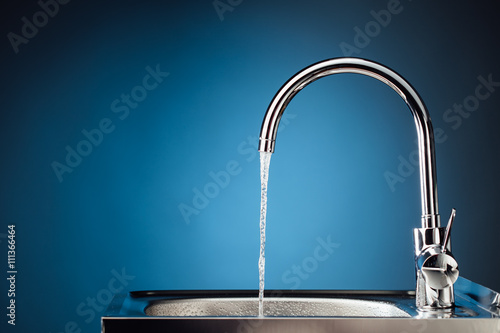 mixer tap with flowing water, blue background